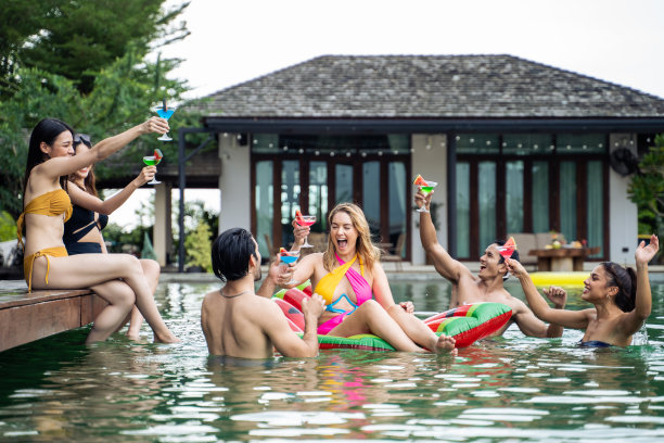 一群不同的朋友一起喝酒，一起开泳池派对。迷人的年轻男子和女子闲逛，庆祝暑假，享受阳光明媚的日子，在私人别墅度假。图片下载