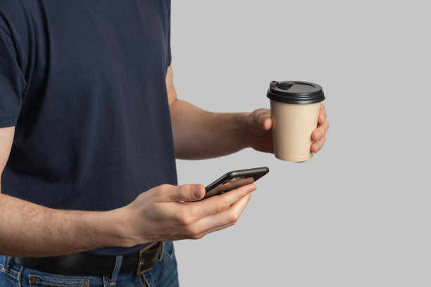 一名欧洲男子手里拿着一部手机，手里拿着咖啡，这是一个灰色的孤立背景图片下载