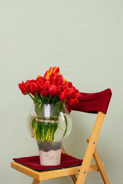 靠墙椅子上的玻璃花瓶里放着一束红色郁金香图片下载