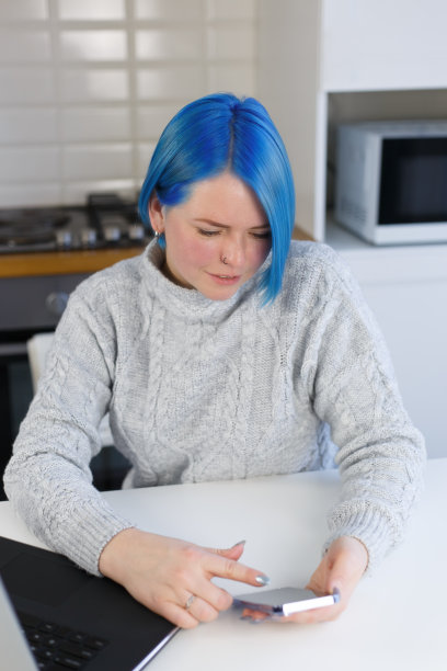 蓝头发的年轻女子在智能手机上浏览移动应用程序。千禧一代女性在家中使用现代手机的俯拍照片图片下载