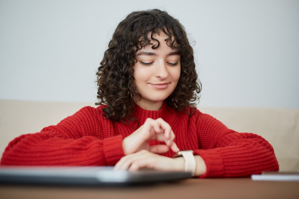 快乐的女学生浏览智能手表上的通知。一个可爱的黑发女性坐在桌子后面，使用现代智能手表小工具图片下载