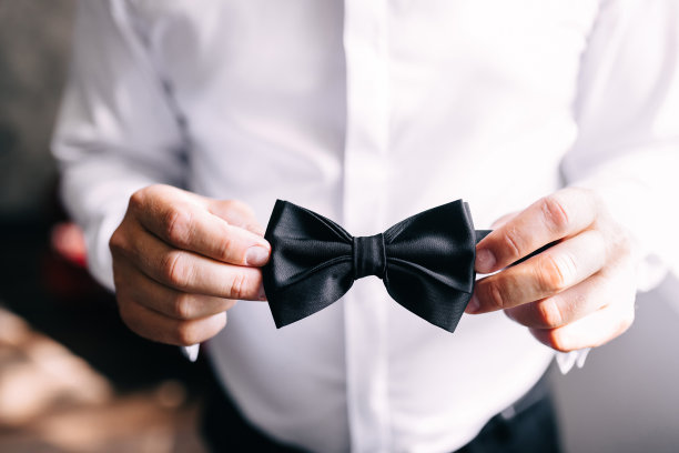 一个穿着白衬衫的年轻人的手的特写，拿着黑色的领结。婚礼的细节图片下载