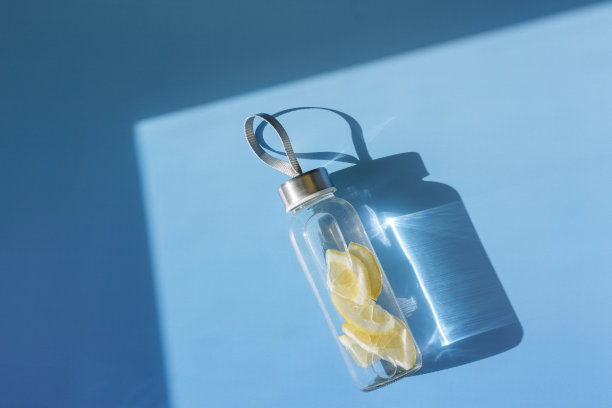 柠檬水喝排毒瓶，硬阴影在阳光下蓝色的背景。养生、饮食、饮食健康的理念。顶景玻璃可重复使用的水瓶，环保的生活方式，最小的照片图片下载