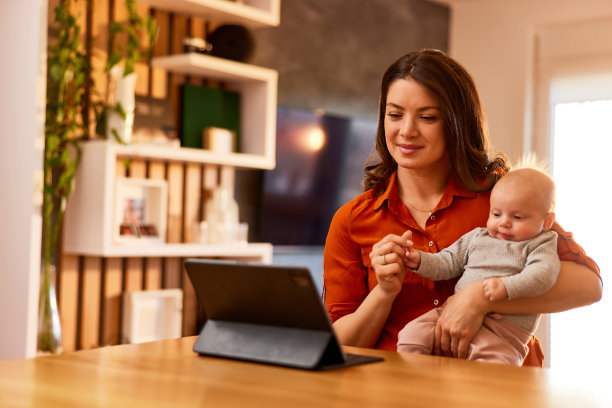 一位漂亮的母亲抱着一个可爱的女婴，在展台上的平板电脑上进行视频通话。图片下载