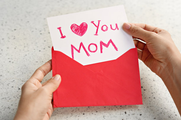 一个女人手里拿着手绘的母亲节贺卡，上面写着“妈妈，我爱你”，手里还握着一个红包。图片下载