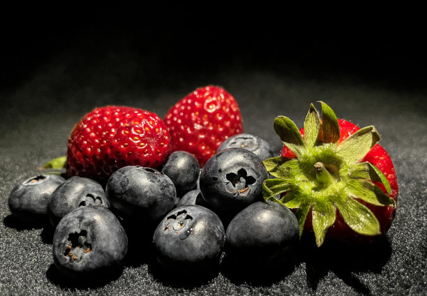 收获甜草莓和蓝莓的特写照片在黑暗的背景。图片下载