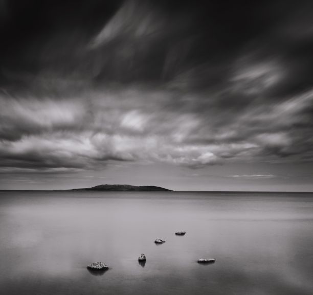 在阴天，远处有一个岛屿的海上岩石的灰度图图片下载