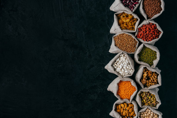 照片中的健康食品成分在小麻袋，孤立的黑色背景与空白的空间，为您的推广。一袋袋的谷物、豆类、水果排在一排图片下载