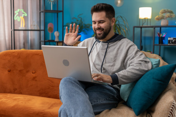 男人坐在家里的沙发上，看着摄像头，与朋友或家人进行视频会议图片下载