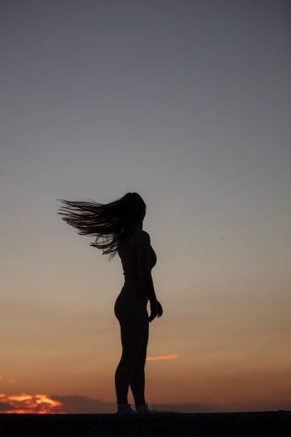 年轻女子的剪影。她在日落时分甩着头发。图片下载