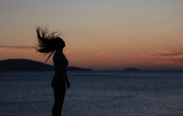 年轻女子的剪影。她在日落时分甩着头发。图片下载