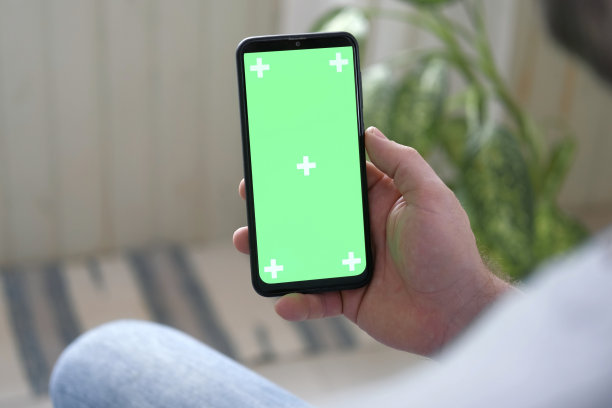 年轻人坐在家里，手里拿着智能手机的绿色模型屏幕。男性使用色度键手机。垂直模式。触摸，滑动显示屏，点击，浏览网络社交媒体图片下载
