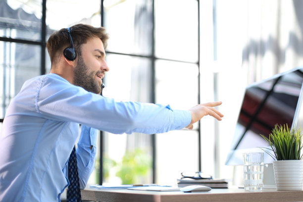 开朗的年轻支持电话男接线员戴着耳机，在工作场所使用电脑，帮助服务和客户咨询呼叫中心的概念。图片下载