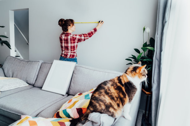 年轻女子正在用卷尺在墙上测量。女孩想把一幅画挂在家里的墙上。家政工作。自己动手修理。DIY，性别平等的工作理念。图片下载