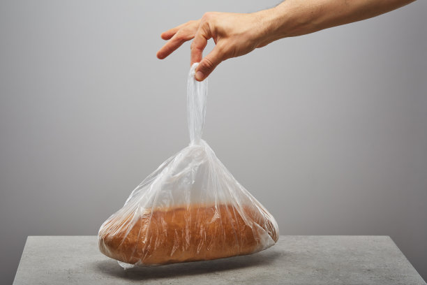 手拿着一个装在塑料袋里的面包放在桌子上图片下载