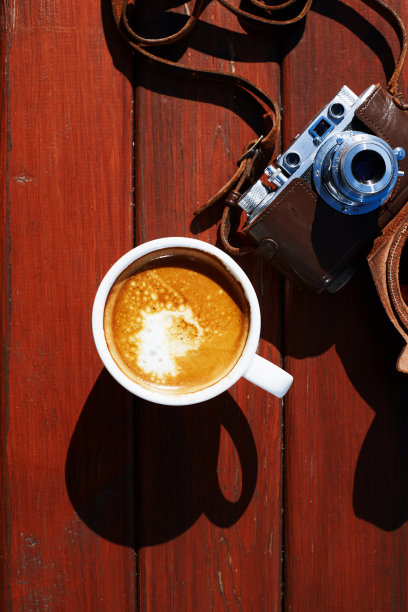 在一个阳光明媚的夏日里，在木桌上的皮革手提箱里的老式胶片相机和一杯咖啡的俯视图图片下载