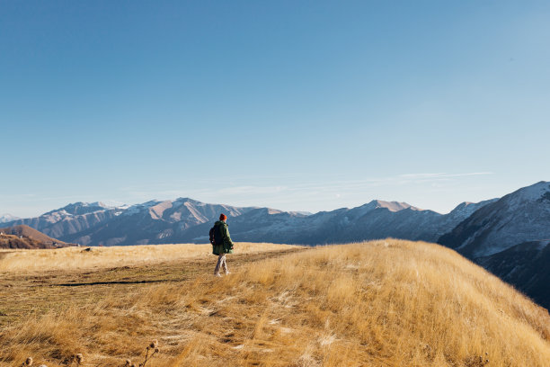 秋天，一个男人在雪峰山的山坡或悬崖上走过一片枯黄的草地图片下载