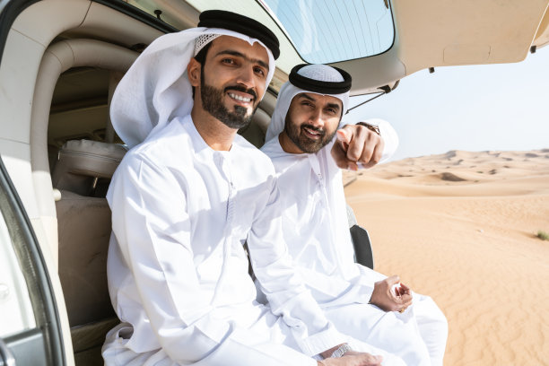 两个中东阿拉伯人穿着阿拉伯坎杜拉在沙漠里开车图片下载