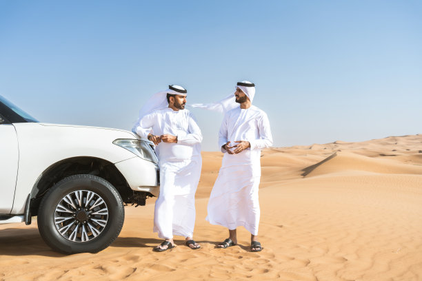 两个中东阿拉伯人穿着阿拉伯坎杜拉在沙漠里开车图片下载