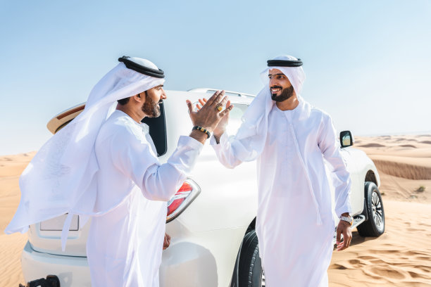 两个中东阿拉伯人穿着阿拉伯坎杜拉在沙漠里开车图片下载
