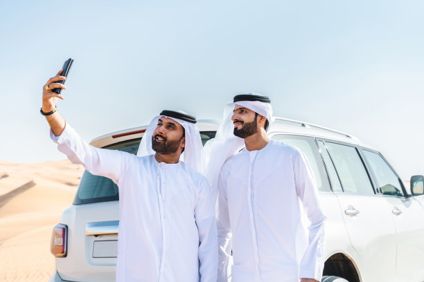 两个中东阿拉伯人穿着阿拉伯坎杜拉在沙漠里开车图片下载