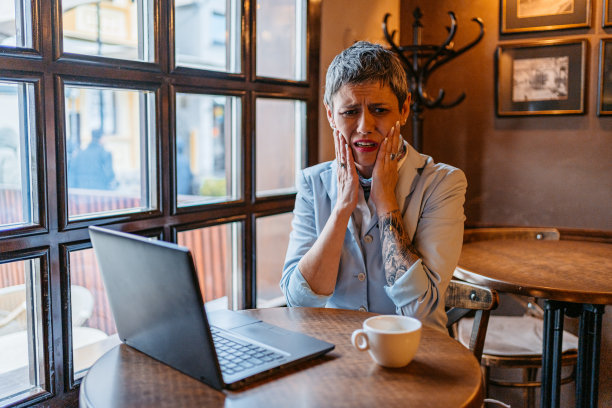 高级女商人在咖啡馆用笔记本电脑工作时牙痛图片下载