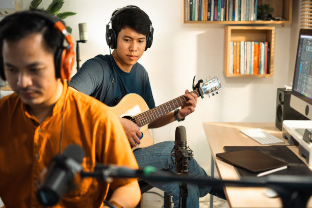 一群亚洲人在家里的录音室里创作音乐。他弹吉他和键盘。图片下载