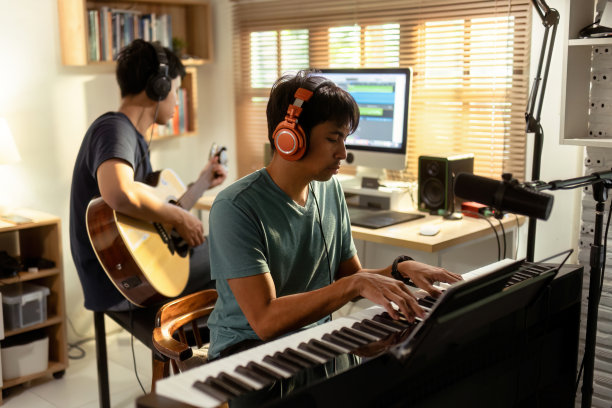 一群亚洲人在家里的录音室里创作音乐。他弹吉他和键盘。图片下载