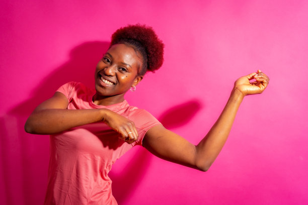 年轻的非裔美国妇女被孤立在粉红色的背景上，微笑着跳舞，摄影棚拍摄图片下载