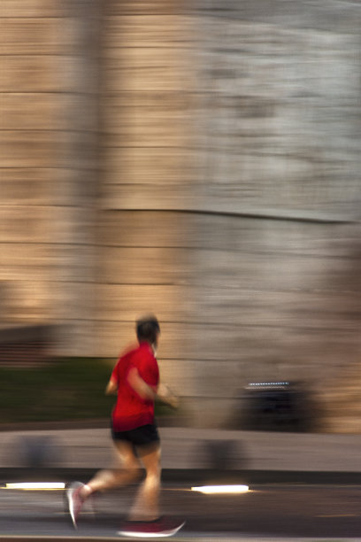 一名身穿红色t恤的男子在日出时奔跑，经过阿根廷国旗纪念碑前，画面模糊。2023年3月。图片下载