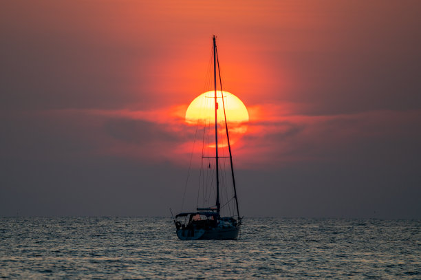 一艘帆船，大大的太阳正落在海中央图片下载