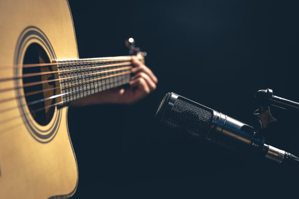 男音乐家在录音棚的麦克风后弹奏原声吉他。图片下载