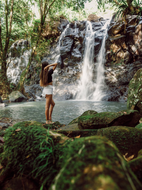 美丽苗条的女人在热带巴厘岛的瀑布上。旅行者女孩在有瀑布的河上摆姿势图片下载
