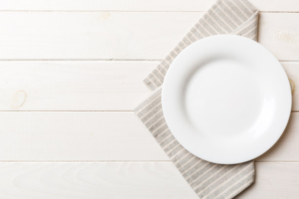 彩色背景上的俯视图，桌布上的空圆形白色盘子盛食物。空盘子放在餐巾上，为你的设计留出空间图片下载