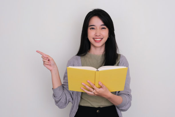 亚洲年轻女子拿着一本书，微笑着指着右边图片下载