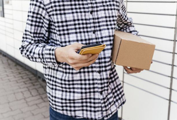 自助邮件终端机旁一个拿着电话的男人。包裹投递机。拿着纸板箱的人。邮件投递和邮政服务，网上购物，电子商务的概念图片下载
