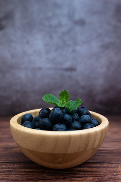 用木碗盛上新鲜蓝莓，再加点薄荷。具有选择性焦点的垂直图像。图片下载