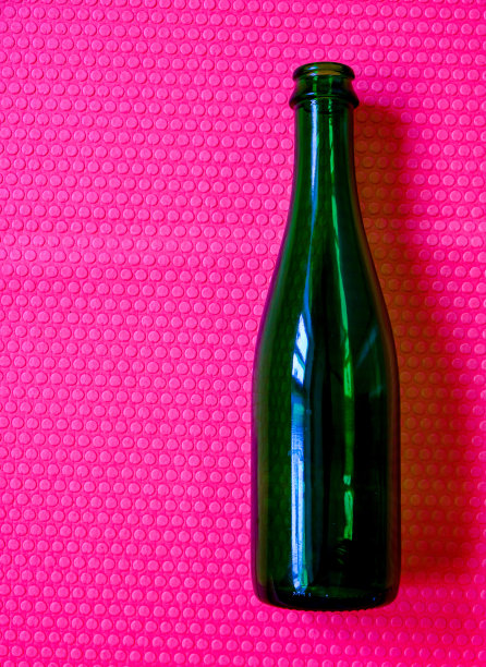 一个空瓶子。亮粉色背景。饮料容器。绿色玻璃。图片下载