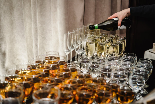 餐饮服务理念。女子将香槟倒入长笛酒杯。人们把香槟倒入酒杯中细细品尝。服务员正在倒白汽酒。瓶子的特写镜头。一排排的满玻璃杯。图片下载