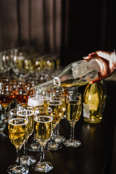 女子将香槟倒入长笛酒杯。人们把香槟倒入酒杯中细细品尝。服务员正在倒白汽酒。瓶子的特写镜头。一排排的满玻璃杯。餐饮服务理念。图片下载