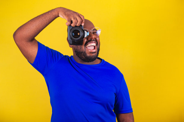 英俊的非洲裔巴西人，戴着眼镜，黄底蓝衬衫。用相机拍照，摄影师，微笑，创意。数码单反相机,图片下载