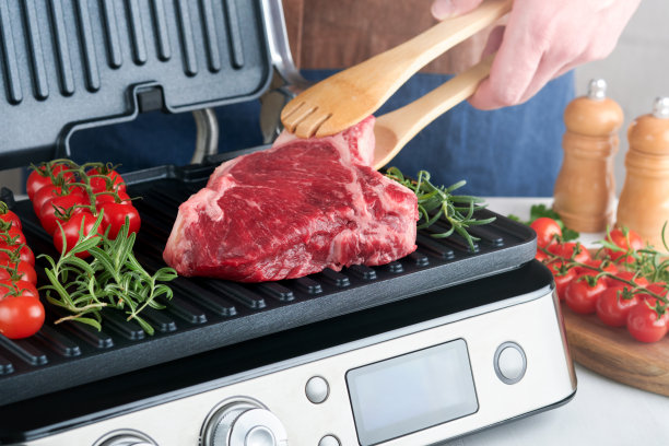 电烤架上的生牛排。厨师男手拿牛排肋眼与迷迭香，樱桃番茄和胡椒在现代电烤架。现代厨房的烹饪过程。俯视图，复制空间。图片下载