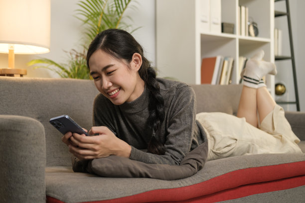 愉快的年轻女子在舒适的沙发上放松，用智能手机在社交网络上聊天。图片下载