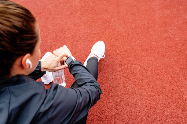 运动中的无线技术。女运动员坐在运动场地的橡胶表面上，使用她的数字腕表。图片下载