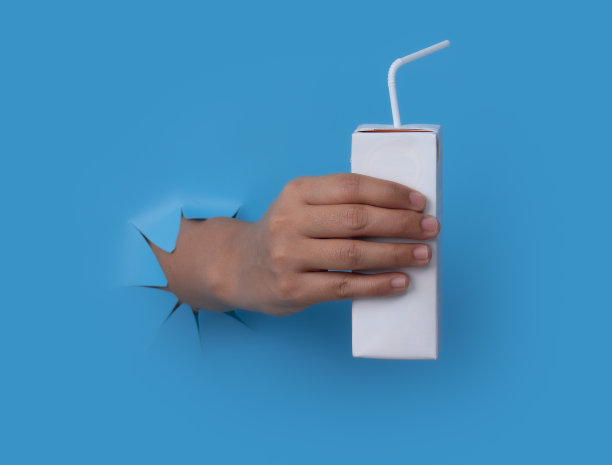 女性的手与空白包装纸箱果汁和牛奶突破蓝纸背景。图片下载