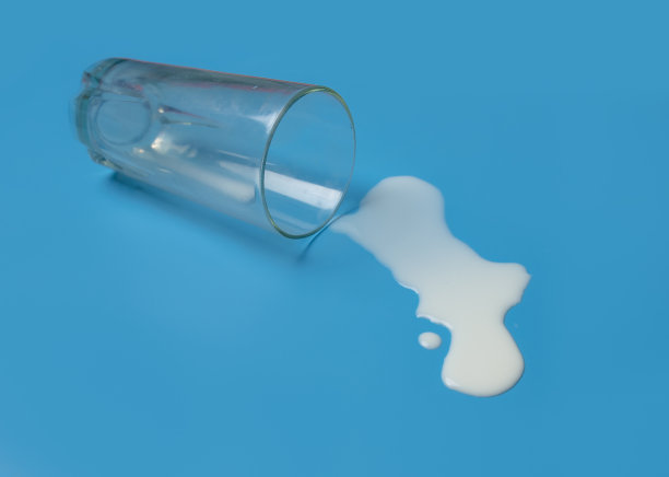 牛奶从玻璃杯里洒出来，洒在蓝色的背景上。图片下载