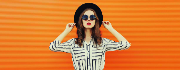 美丽的年轻女子的肖像，穿着白色条纹衬衫，在橙色背景上戴着黑色圆帽图片下载