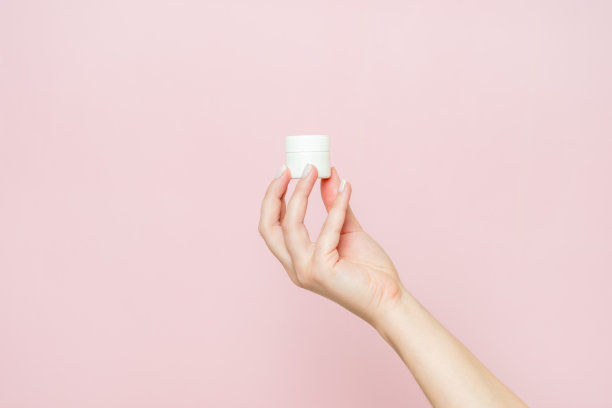 白色的罐子或管，手里拿着奶油(药膏)。面部护理，瓶装化妆品无标签。图片下载