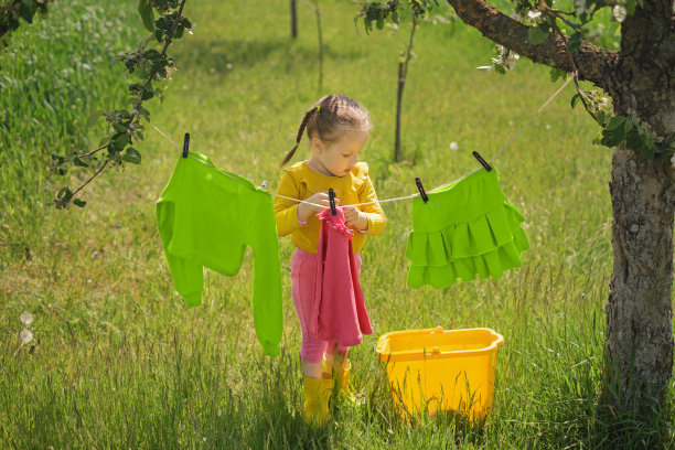 一个扎着小辫子的女孩把一件t恤用衣夹挂在晒衣绳上。图片下载