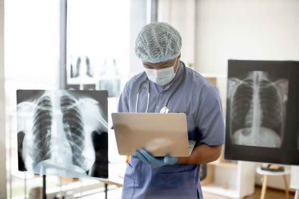 戴着口罩和手术服的医生通过笔记本电脑检查x光扫描图片下载